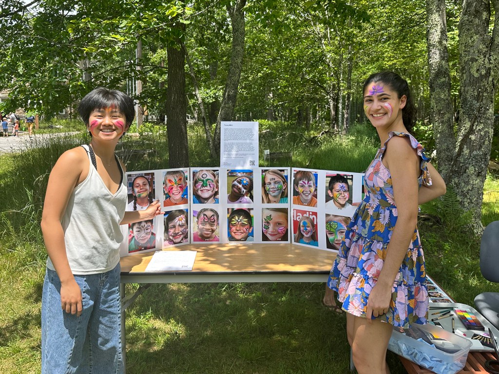 Two children with face paint beside the design board for AI Face Paint, 2023, by Matt King. Participatory face-painting performance.