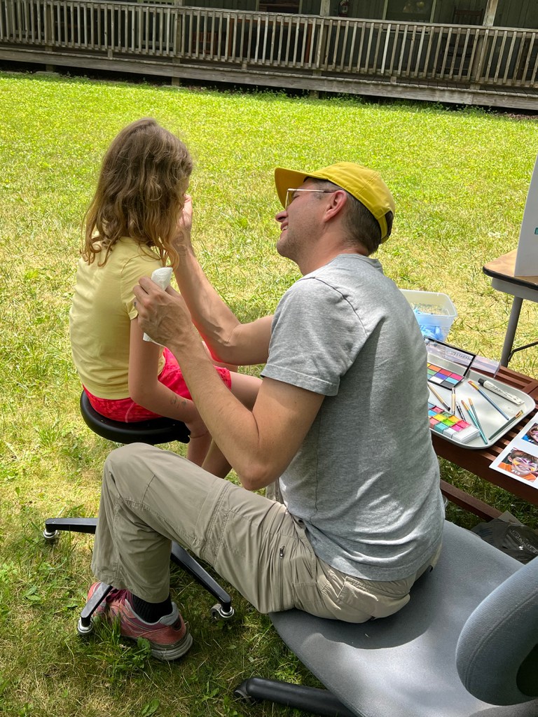 Matt King painting a child’s face for AI Face Paint, 2023, by Matt King. Participatory face-painting performance.